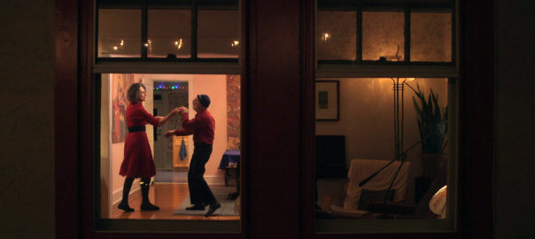 A man and a woman are dancing as seen through a window