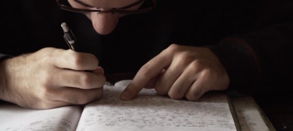 A man leans over a lined sheet of paper and draws