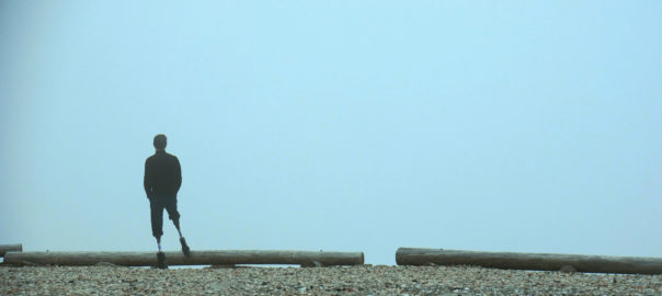 A man with two prosthetic legs looks out over a foggy cliff