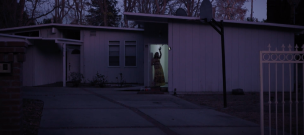 A woman stands silhouetted in a doorway to a house