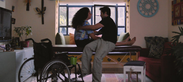A woman receives physical therapy on a table. A wheelchair sits in the corner.