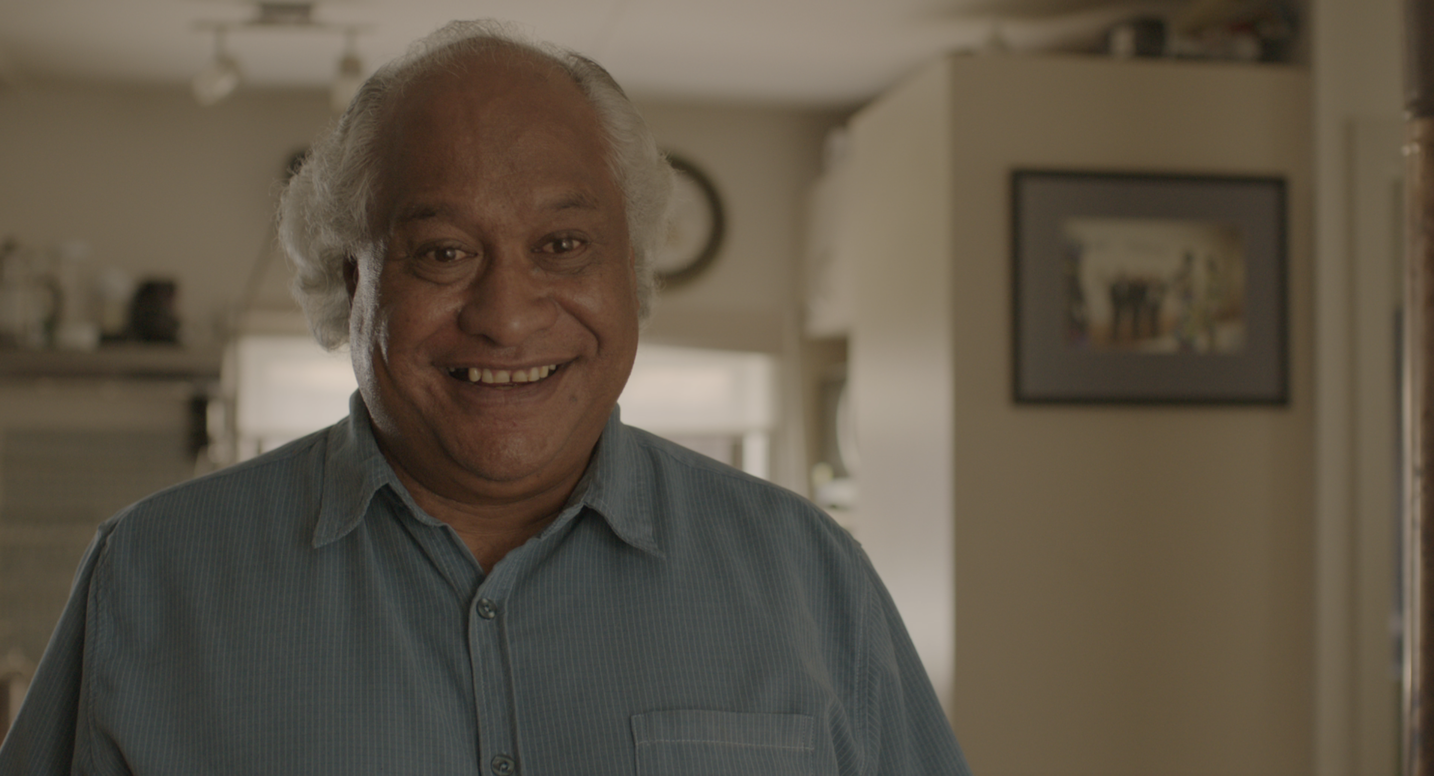 An older man smiles. He is wearing a blue shirt.