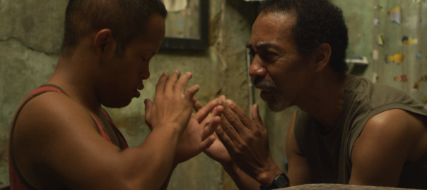 A young man and his father play a hand game. They are both wearing tank tops