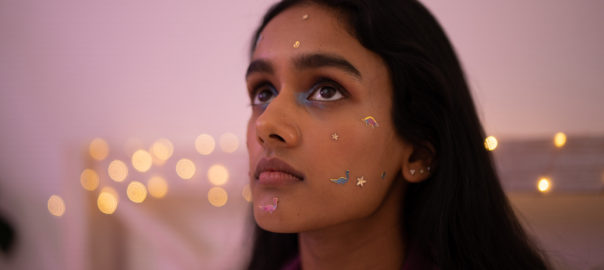 A woman with long dark hair, her face decorated with colorful stickers.