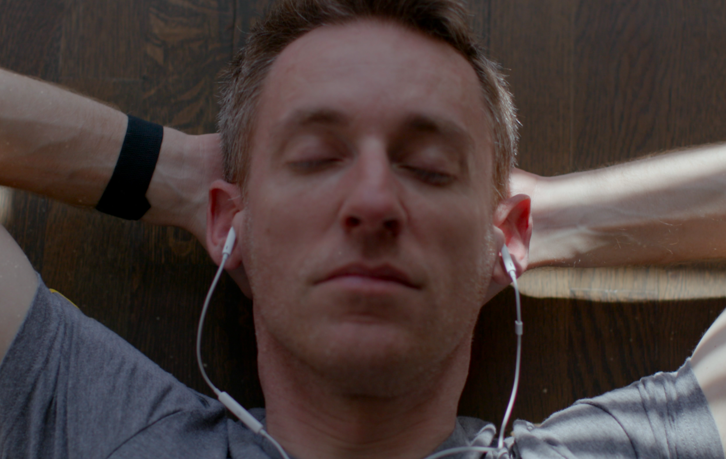 A man wearing headphones rests his arms behind his head with his eyes closed.