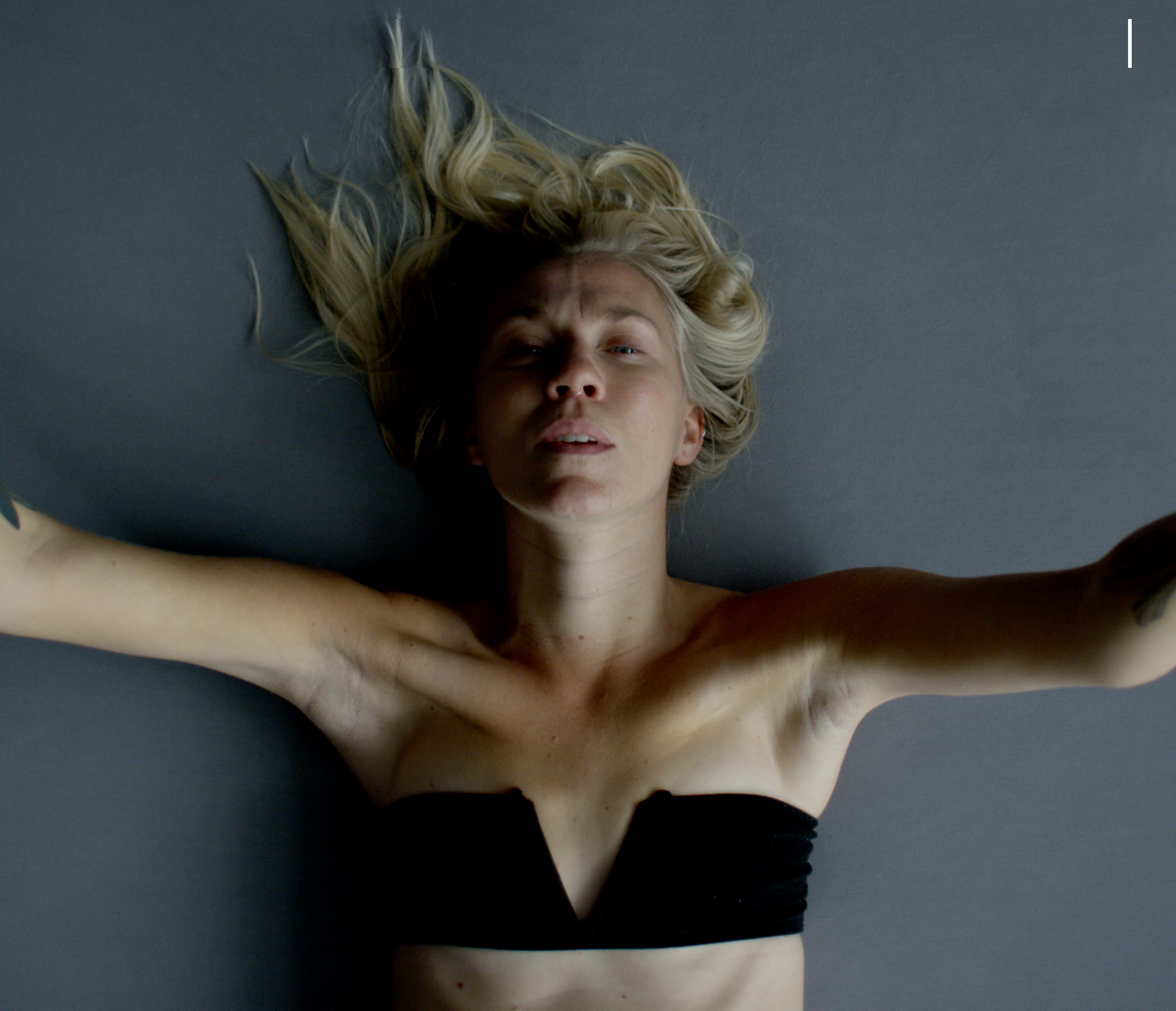 Dancer Kelsey Peterson, wearing a dark black bra, lies on her back with her arms outstretched.