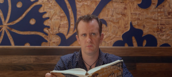 a man looking up from a book that he is holding, titled "amazing adventures"