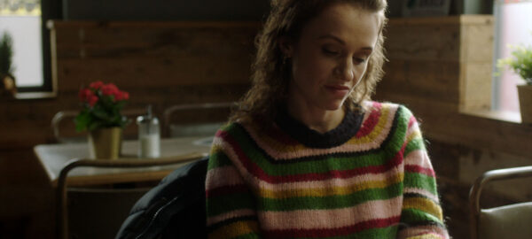 a woman sitter at a diner, gazing at the coffee mug she is holding in both hands