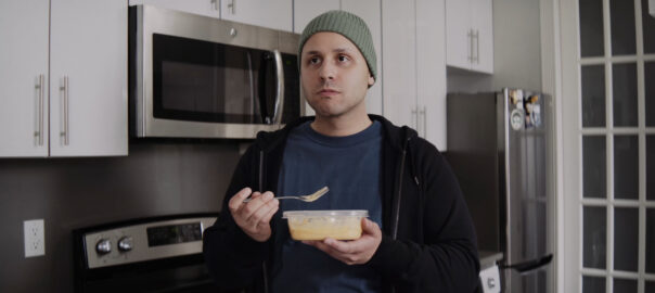 a young man standing in the kitchen, holding a food container and a fork in his hands