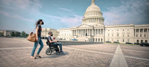 A man in a wheelchair and a woman, facing to the US Capitol building