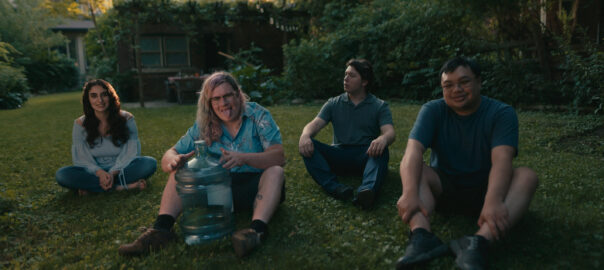 3 young men and one woman sitting on the grass looking to the camera