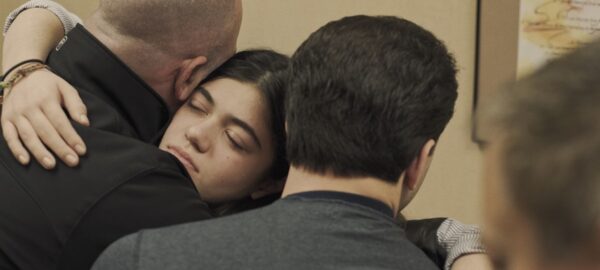 A young woman embraces two men in her arms.