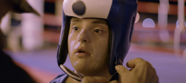a young man with Down syndrome is being helped to tighten up a boxing head-protecting gear