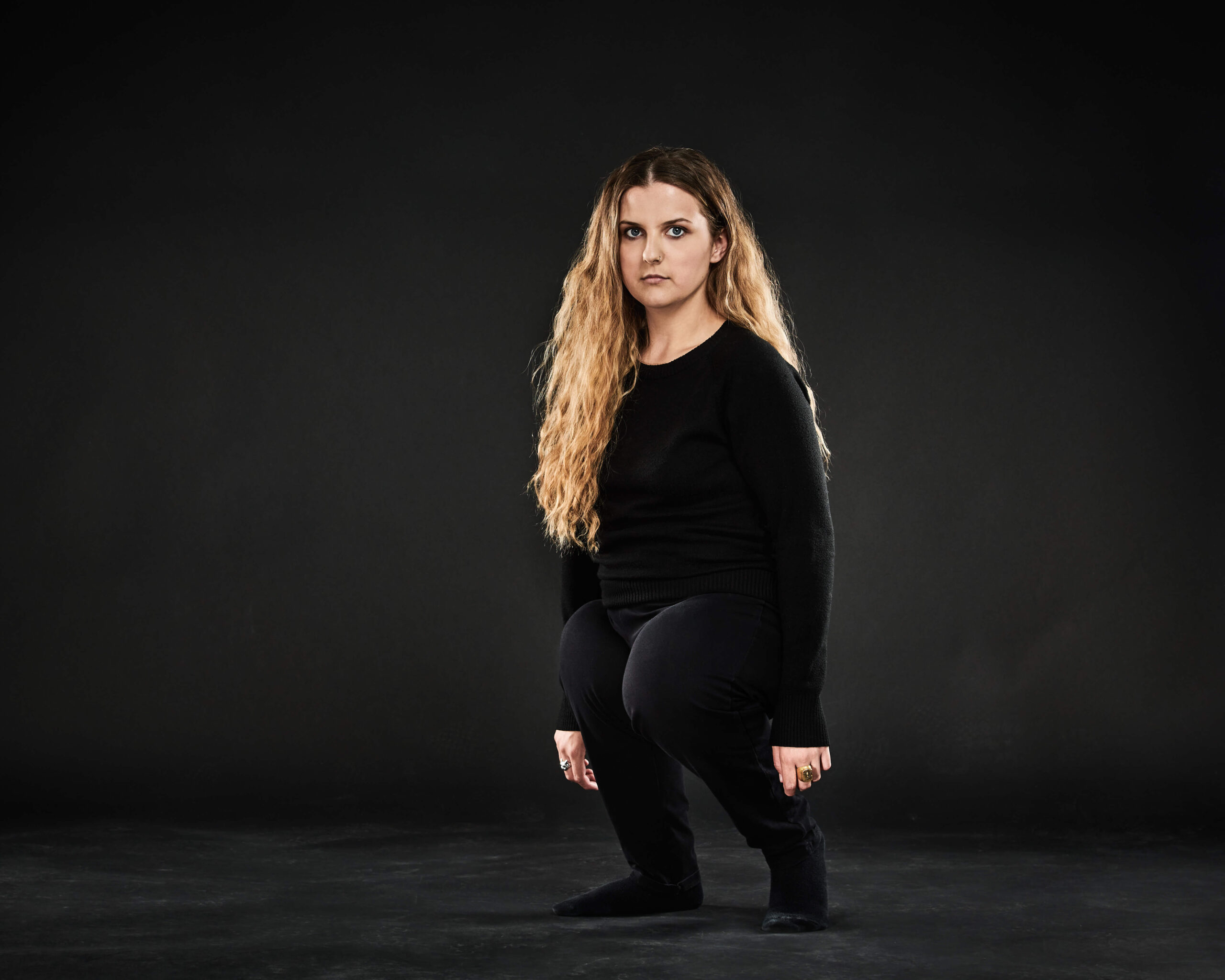 A woman in a black shirt with shorter legs looks into the camera with a piercing gaze.