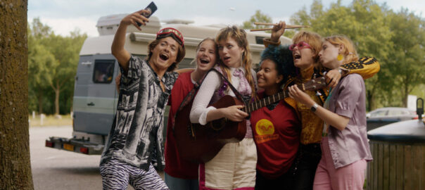 A group of teens stand with a guitar and pose for a group selfie.